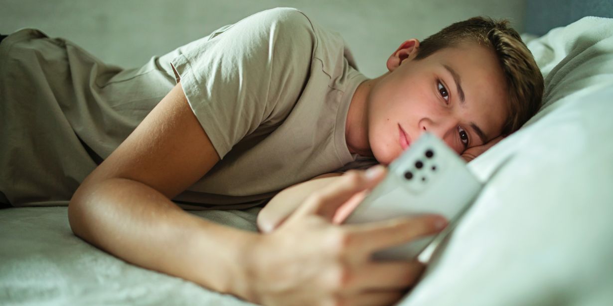 Jugendlicher mit Handy im Bett